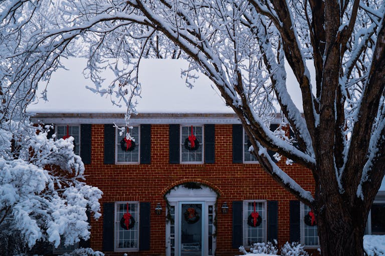A cozy brick house adorned with holiday wreaths on a snowy winter day.